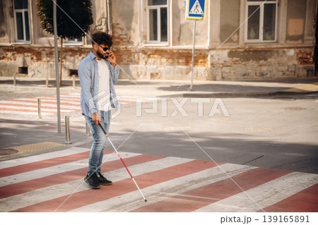 Crossing the road. Blind man with white cane and sunglasses is in the city Crossing the road. Blind man with white cane and sunglasses is in the city 139165891