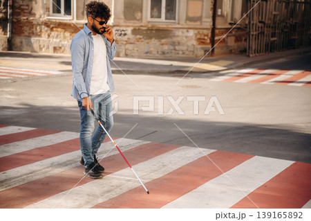 Crossing the road. Blind man with white cane and sunglasses is in the city Crossing the road. Blind man with white cane and sunglasses is in the city 139165892