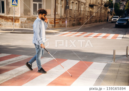 Side view, walking. Blind man with white cane and sunglasses is in the city 139165894