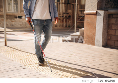 Walking on the pavement. A blind man with white cane is in the city 139165896