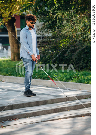 Side view, walking. Blind man with white cane and sunglasses is in the city Side view, walking. Blind man with white cane and sunglasses is in the city 139165910