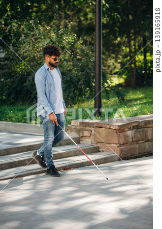 Side view, walking. Blind man with white cane and sunglasses is in the city 139165918