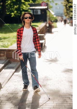 Front view, walking. Blind young guy is in the town outdoors Front view, walking. Blind young guy is in the town outdoors 139166147