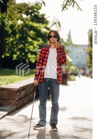 White cane is in hand. Blind young guy is in the town outdoors 139166153
