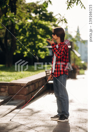 Smartphone in hand, talking. Blind young guy is in the town outdoors 139166155