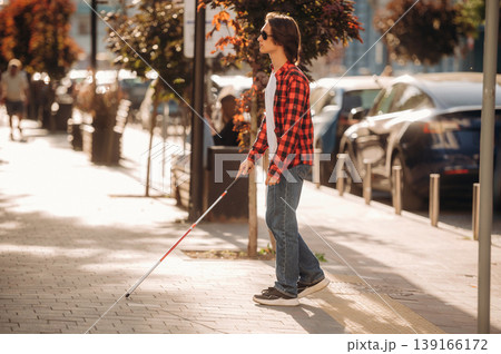 The practical use of white cane. Blind young guy is in the town outdoors The practical use of white cane. Blind young guy is in the town outdoors 139166172