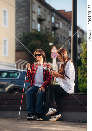 Smiling, enjoying the story. Woman is reading the book for blind guy, sitting outdoors 139166179