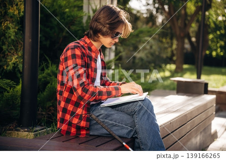Reading the book using Braille technique. Blind young guy is in the town outdoors Reading the book using Braille technique. Blind young guy is in the town outdoors 139166265