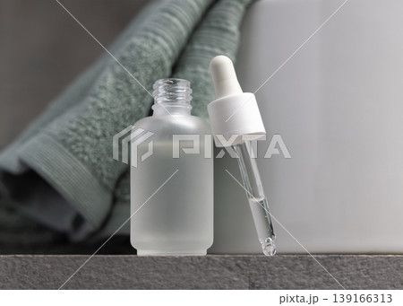 Pipette set near an opened glass dropper bottle against sage green towel in bathroom. Spa concept 139166313