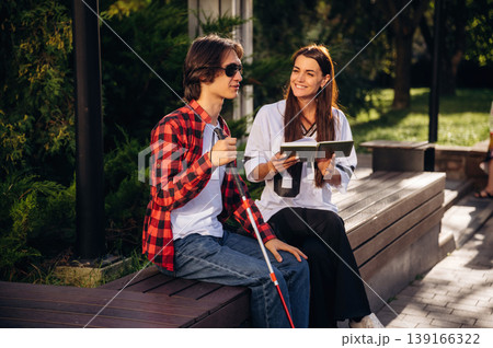 Woman is reading the book for blind guy, sitting outdoors 139166322