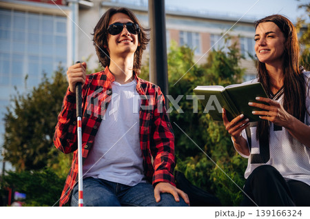 Smiling, enjoying the story. Woman is reading the book for blind guy, sitting outdoors 139166324