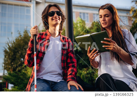 Smiling, enjoying the story. Woman is reading the book for blind guy, sitting outdoors 139166325
