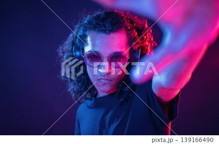 Performance of DJ, in headphones. Guy is indoors at night with neon lighting Performance of DJ, in headphones. Guy is indoors at night with neon lighting 139166490