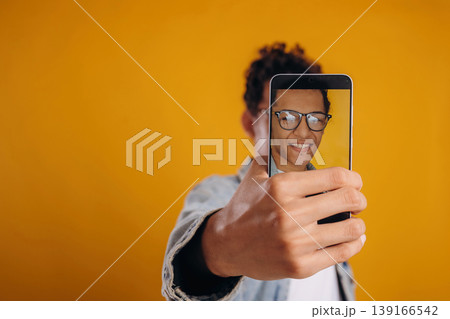 Making photo of himself by smartphone. Young guy is against yellow background 139166542