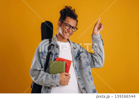 Guitar backpack on back and notepads in hand. Young guy is against yellow background 139166544