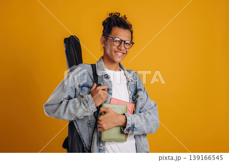 Guitar backpack on back and notepads in hand. Young guy is against yellow background Guitar backpack on back and notepads in hand. Young guy is against yellow background 139166545