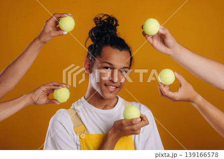Hands are holding tennis balls, sport conception. Young guy is against yellow background Hands are holding tennis balls, sport conception. Young guy is against yellow background 139166578