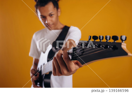Electric guitar player is standing. Young guy is against yellow background 139166596