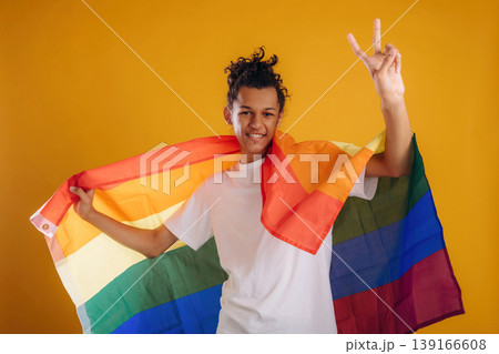 LGBT flag is in hands, supporting the pride community. Young guy is against yellow background 139166608
