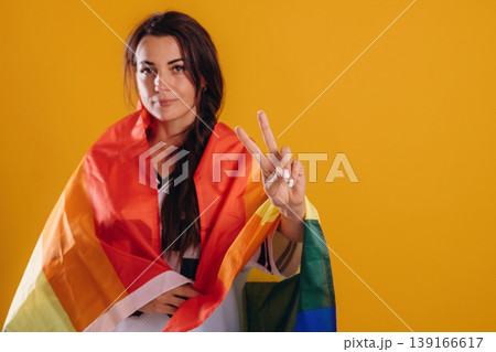 Woman is standing with LGBT flag against yellow background Woman is standing with LGBT flag against yellow background 139166617