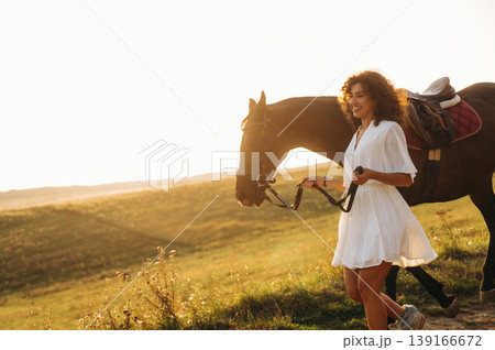 The walk on the footpath. Woman in white dress is with horse on the countryside field 139166672