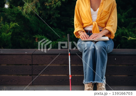Blind woman with white cane is sitting and reading the book using Braille language and technique Blind woman with white cane is sitting and reading the book using Braille language and technique 139166703
