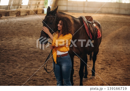 Yellow colored natural sunlight, standing and posing. Beautiful young woman is with horse in hangar 139166719