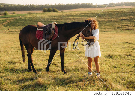 Warm season, farming conception. Woman in white dress is with horse on the countryside field Warm season, farming conception. Woman in white dress is with horse on the countryside field 139166740