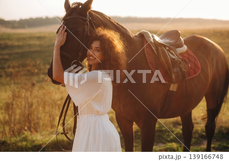 Woman in white dress is with horse on the countryside field 139166748