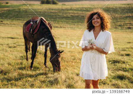 Grass is in hands. Woman in white dress is with horse on the countryside field Grass is in hands. Woman in white dress is with horse on the countryside field 139166749