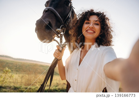 Making a selfie. Woman in white dress is with horse on the countryside field Making a selfie. Woman in white dress is with horse on the countryside field 139166773
