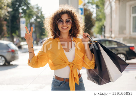 Showing hand gesture. Happy woman is with shopping bags in town Showing hand gesture. Happy woman is with shopping bags in town 139166853