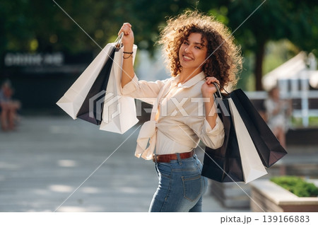Brown curly hair. Happy woman is with shopping bags in town Brown curly hair. Happy woman is with shopping bags in town 139166883