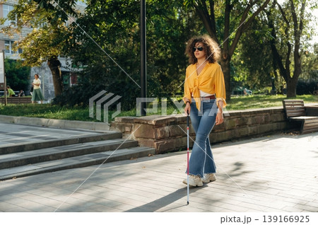 Having a walk, using white cane. A blind woman is in the modern city at daytime 139166925
