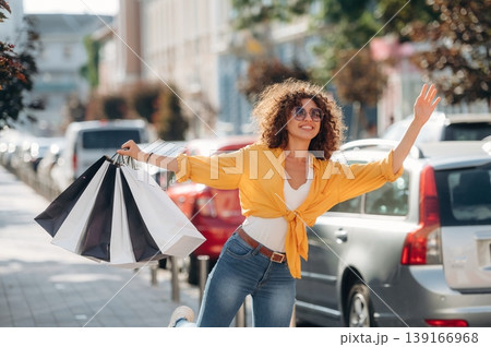Calling the taxi with hand gesture. Happy woman is with shopping bags in town 139166968