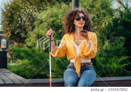 Talking by phone. A blind woman is in the modern city at daytime Talking by phone. A blind woman is in the modern city at daytime 139167002