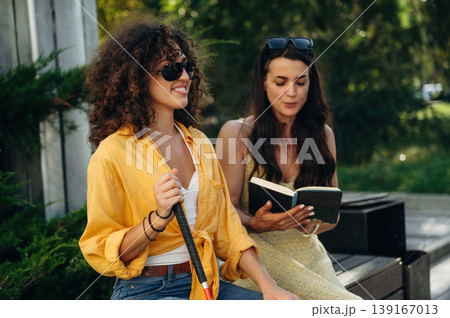 Woman is reading the book for a blind person, sitting outdoors in the public park 139167013