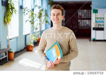 Happy male student standing in the campus in sunny day holding books, exercise books, happy to study in university and have high academic performance 139167710