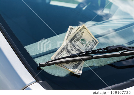 Bundle of US dollar banknotes left on a car under the car wiper on a windscreen Bundle of US dollar banknotes left on a car under the car wiper on a windscreen 139167726