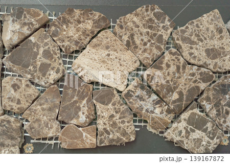 Close-up of irregular brown stone mosaic tiles arranged on mesh backing. Natural texture with organic shapes and earthy tones, ideal for flooring, wall design, or architectural backgrounds. Close-up of irregular brown stone mosaic tiles arranged on mesh backing. Natural texture with organic shapes and earthy tones, ideal for flooring, wall design, or architectural backgrounds. 139167872