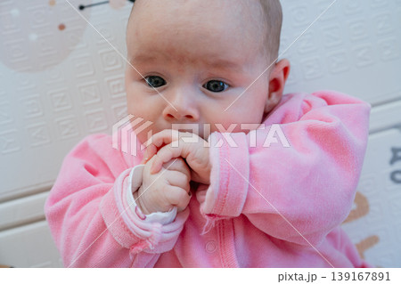 Baby girl in pink outfit lying and sucking fingers. Childhood and development concept. Baby girl in pink outfit lying and sucking fingers. Childhood and development concept. 139167891