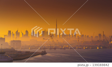 Dubai, United Arab Emirates - Jan 12 2024, Panoramic view of downtown Dubai skyscrapers, with Burj Khalifa, at dawn in a haze, with port and ship on foreground, Dubai, United Arab Emirates Dubai, United Arab Emirates - Jan 12 2024, Panoramic view of downtown Dubai skyscrapers, with Burj Khalifa, at dawn in a haze, with port and ship on foreground, Dubai, United Arab Emirates 139169842