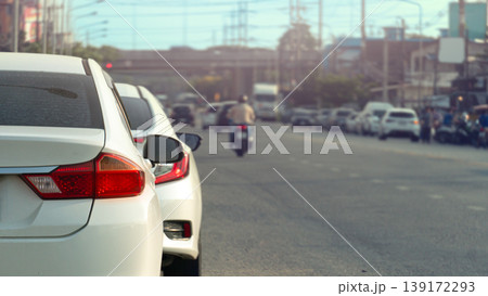 Rear side of whtie car driving on the aspahtl road. Light traffic in rural towns. Reveals cars parked along the side of the road. city with tangled streetlights and cables. Under blue sky. 139172293