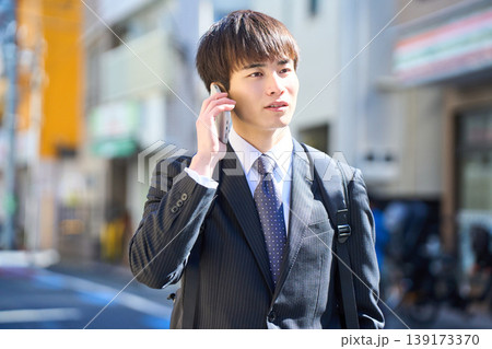 外回りの営業中に街中で電話対応をする若い日本人ビジネスマン 外回りの営業中に街中で電話対応をする若い日本人ビジネスマン 139173370