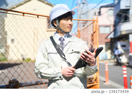 タブレットを手に持ち建設現場の状況を確認する男性現場監督 139173439