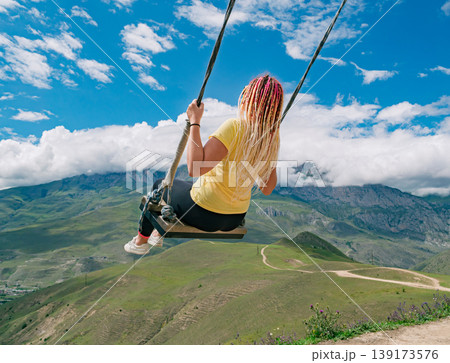Woman enjoying mountain swing ride overlooking the valley with vast green landscapes of Caucasus Mountains and blue sky Woman enjoying mountain swing ride overlooking the valley with vast green landscapes of Caucasus Mountains and blue sky 139173576