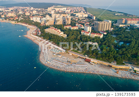 Warm summer afternoon at a popular resort city beach with many people swimming and sunbathing Warm summer afternoon at a popular resort city beach with many people swimming and sunbathing 139173593