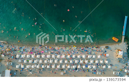 Aerial view of a vibrant beach filled with bathers enjoying warm water and sun under white umbrellas Aerial view of a vibrant beach filled with bathers enjoying warm water and sun under white umbrellas 139173594
