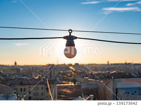 Warm glow of a setting sun highlighting a lone light bulb above a sprawling urban landscape 139173642