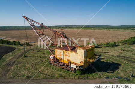 Massive industrial dragline excavator rests in an open field, surrounded by sparse vegetation and dirt roads Massive industrial dragline excavator rests in an open field, surrounded by sparse vegetation and dirt roads 139173663